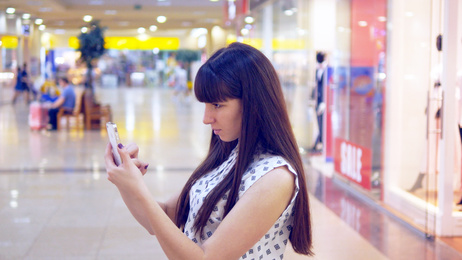 Young woman playing Pokemon GO indoor at shopping center, using smart phone. Girl play the popular smartphone game - catching pokemon in hypermarket mall