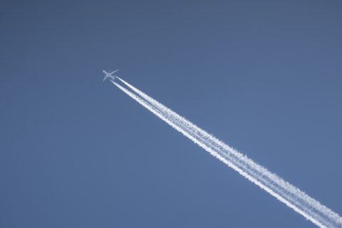Commercial two engines jet airliner flies high in clear sky leaving bright white trace